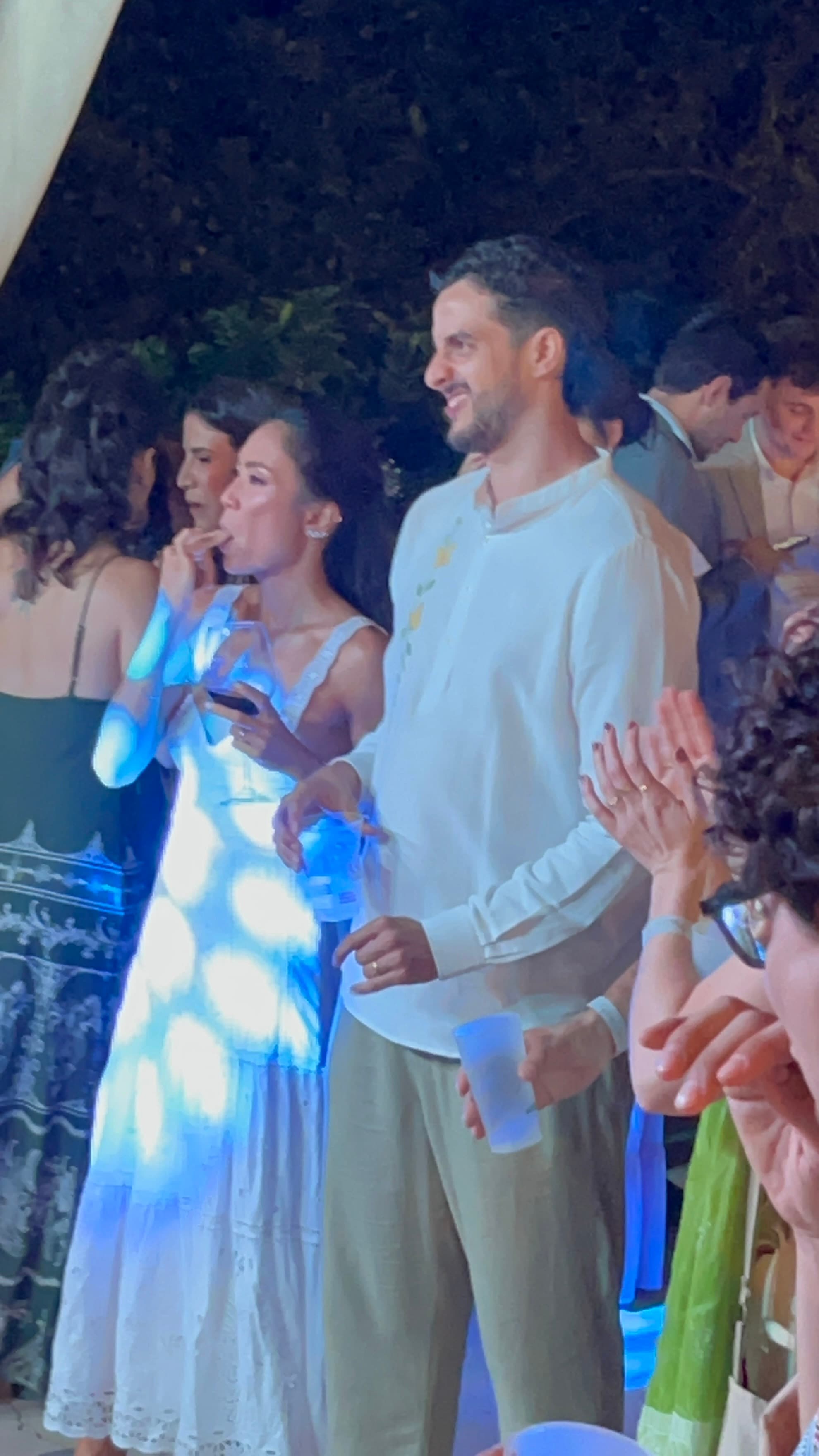 Homem e mulher em festa noturna com luzes azuis, segurando bebidas e vestindo roupas claras.