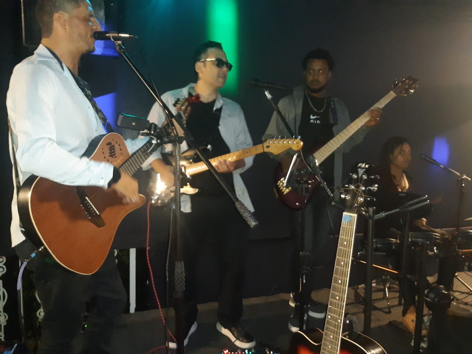 Banda musical se apresentando ao vivo em palco com guitarras, baixo e bateria sob luzes.